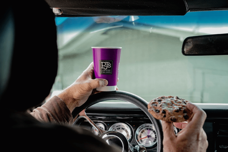 Man driving car while holding PJ's Coffee to-go cup and cookie